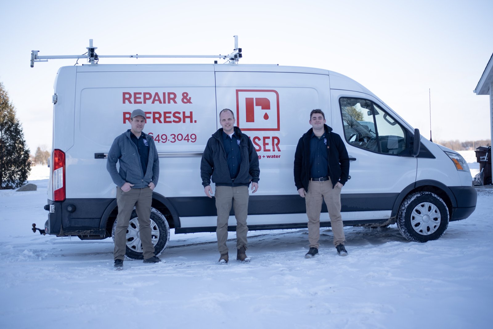 The Riser Plumbing + Water crew standing beside a Riser service van in the snow