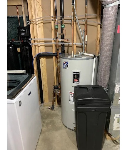 A tank water heater in a basement next to a water softener